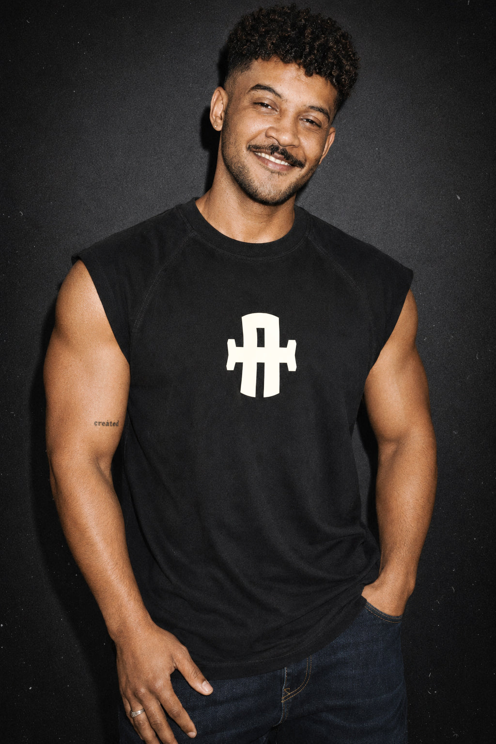 Man wearing a black sleeveless shirt with a white logo on a dark background