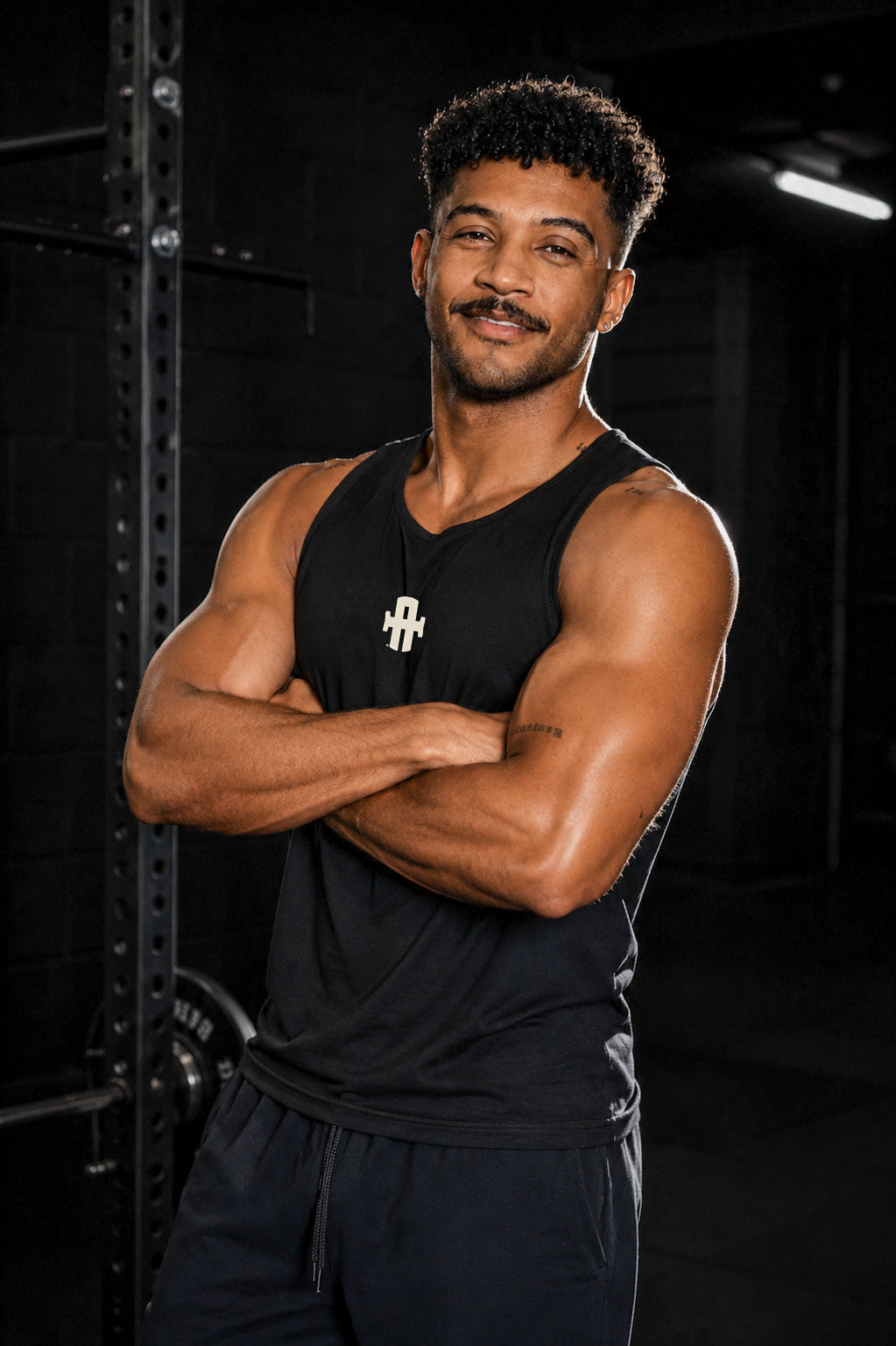 Man wearing a black tank top with a logo, standing in a dark indoor setting.