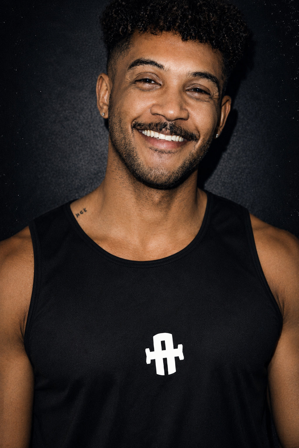 Man wearing a black tank top with a logo on a dark background