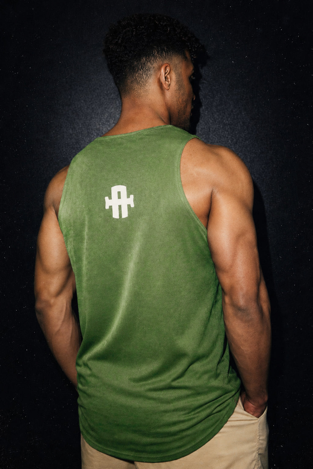 Person wearing a green tank top with a white logo on the back against a black background