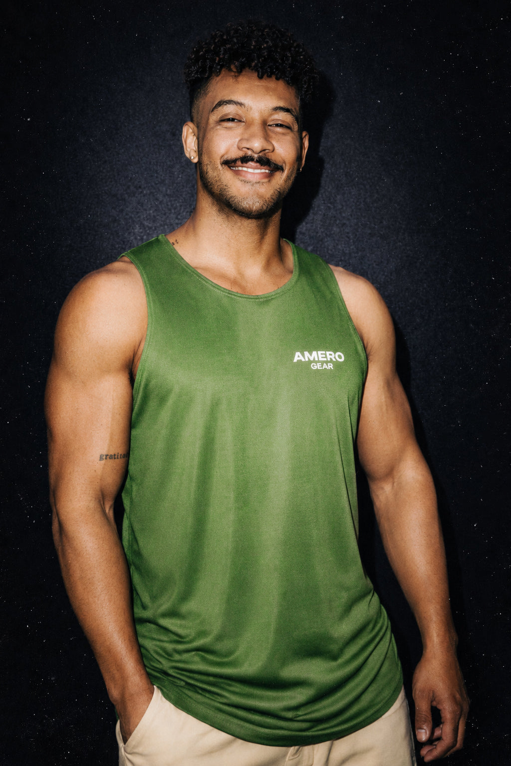 Man wearing a green tank top with 'Amero Gear' logo against a dark background